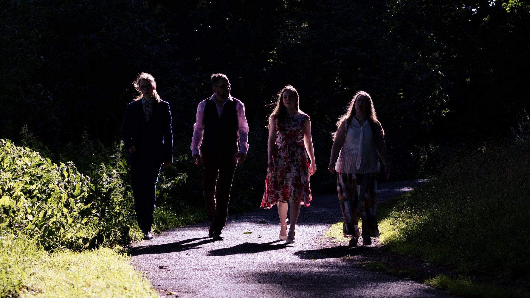 Four wedding guests walking along a shaded path, backlit by late afternoon sun