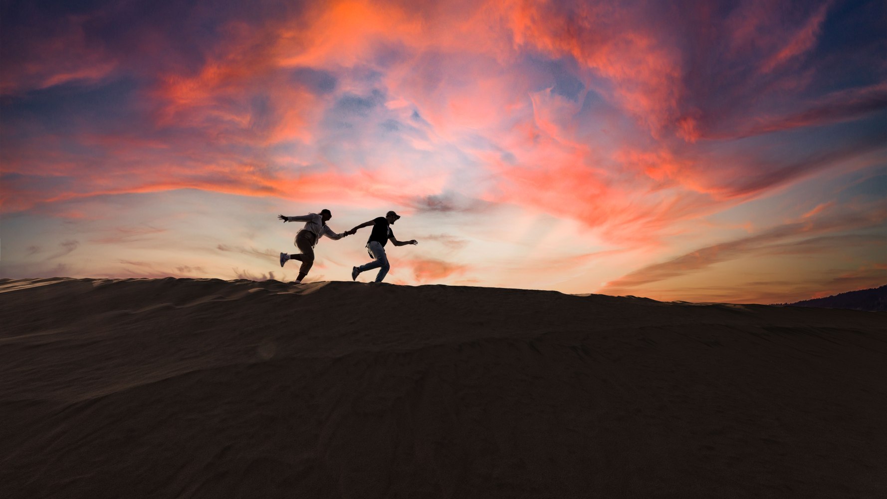 Two people running along a dune ridge at sunset