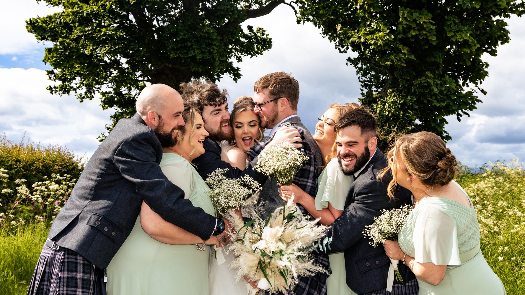 The wedding party in a group hug and laughter under a tree