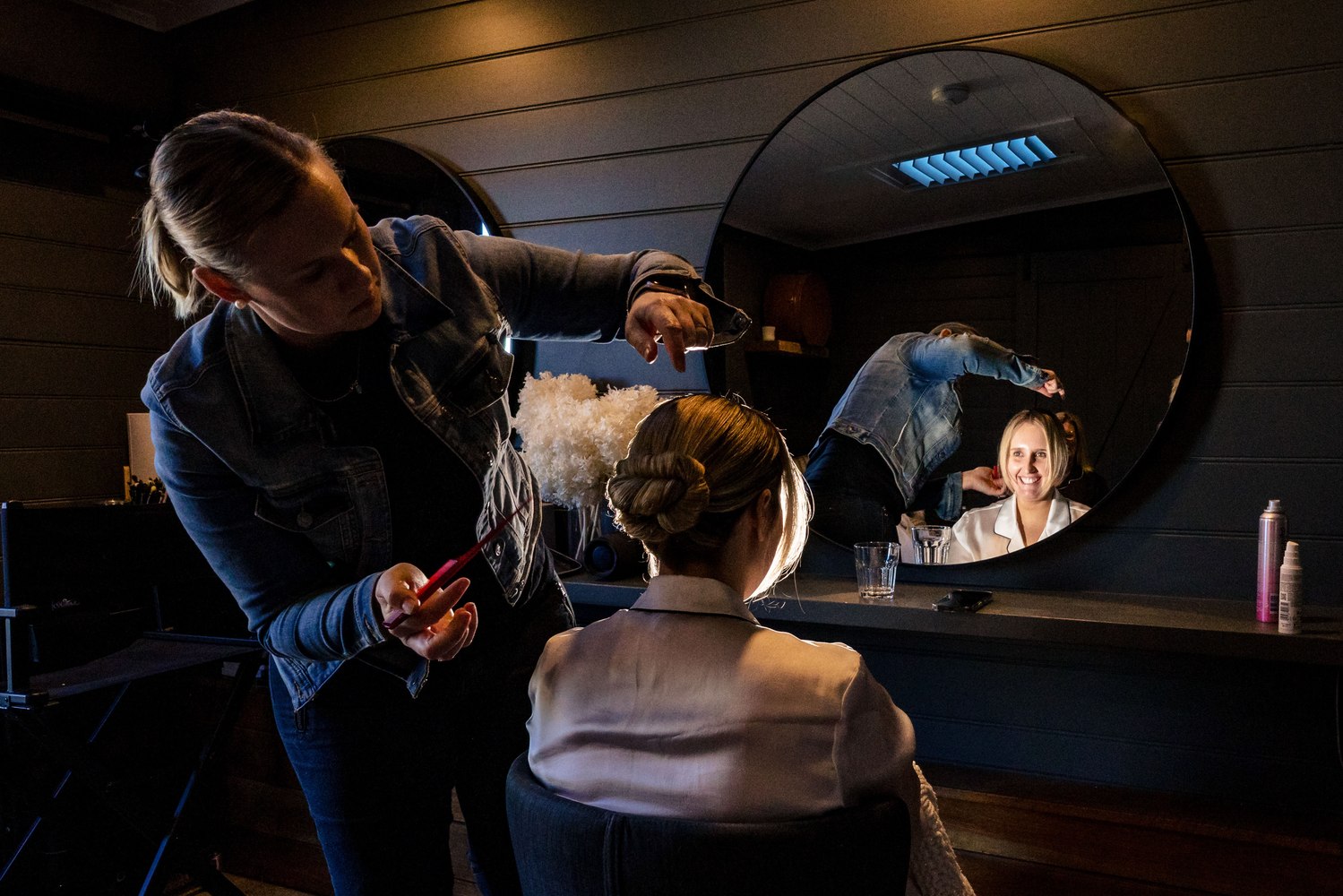 A stylist finishing the bride's hair, reflected in a round mirror