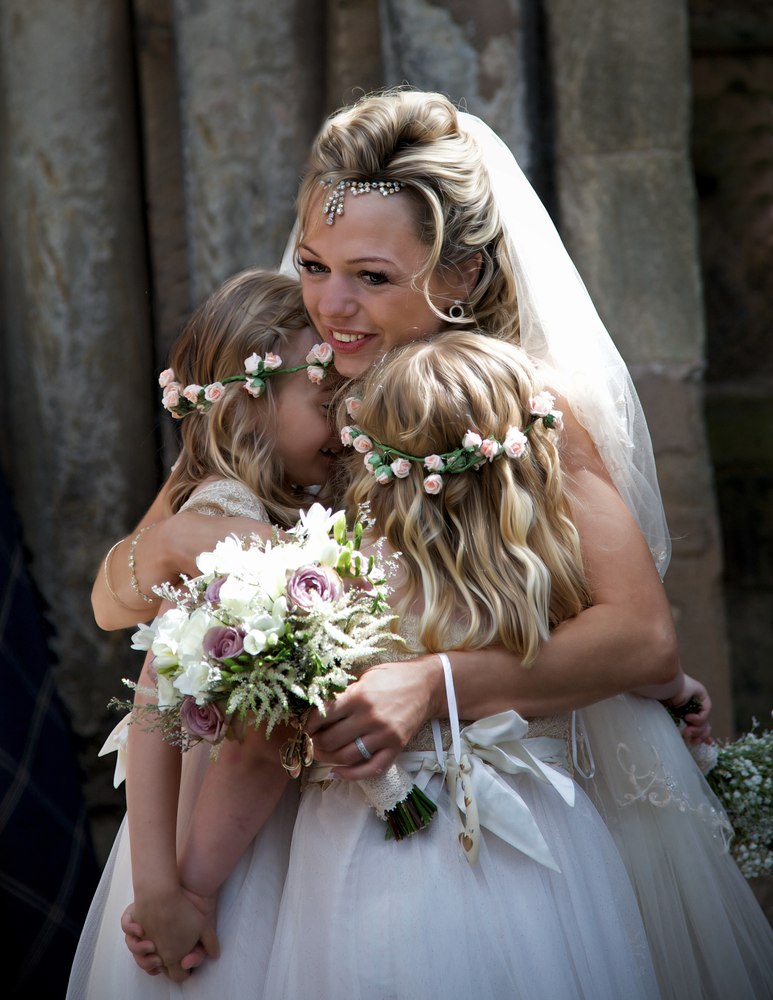 Bride hugging her two flower girls, all wearing flower crowns