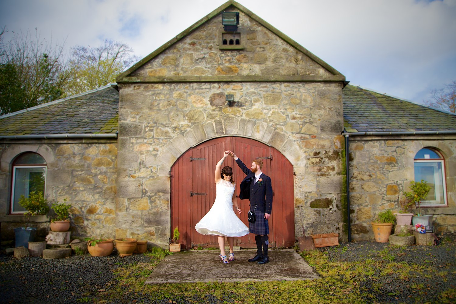 Bride and groom dancing in front of an old stone barn