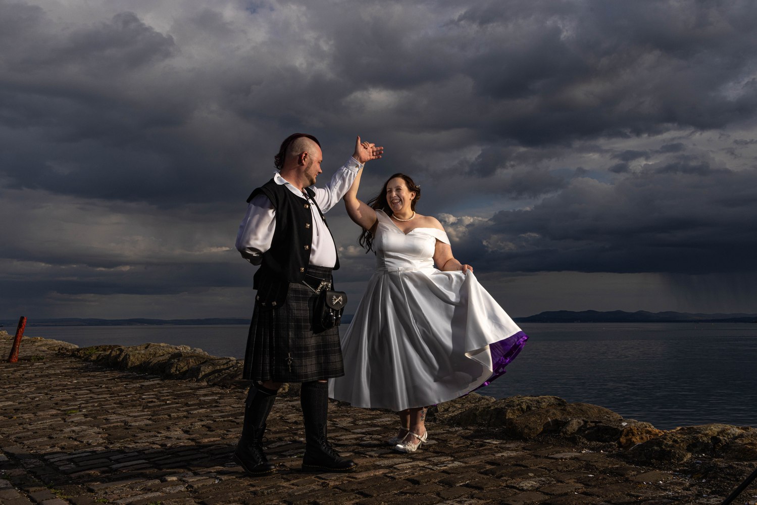 Bride and groom dancing on a stormy pier, groom in a kilt
