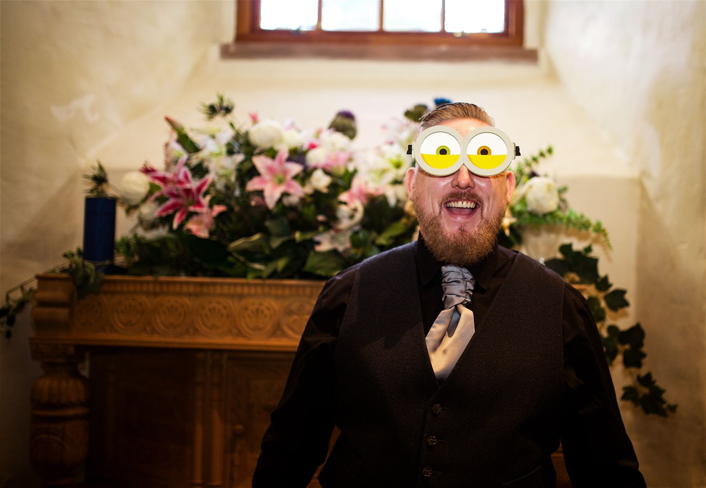 A groomsman clowning around in novelty glasses beside the church flowers