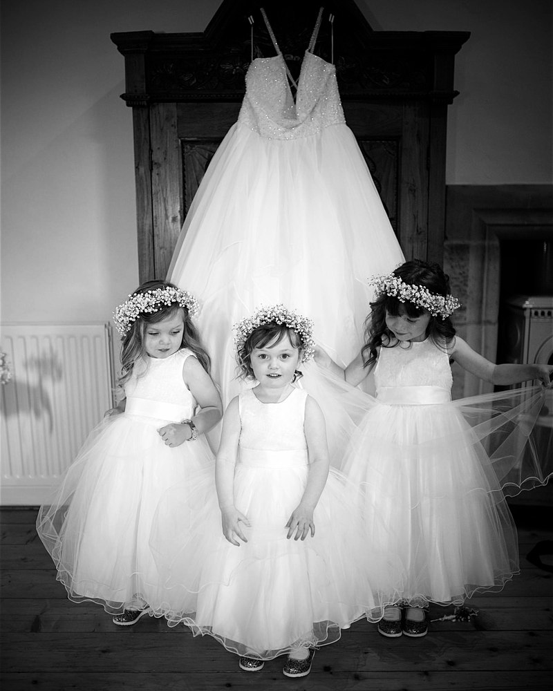 Three flower girls in flower crowns in front of the hanging wedding dress