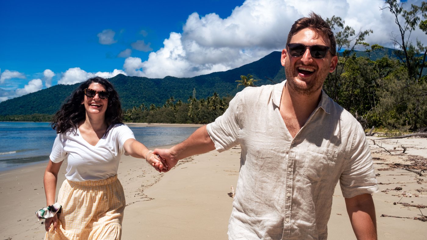 Lukas and Marianna running hand in hand along the sand, rainforest mountains behind them