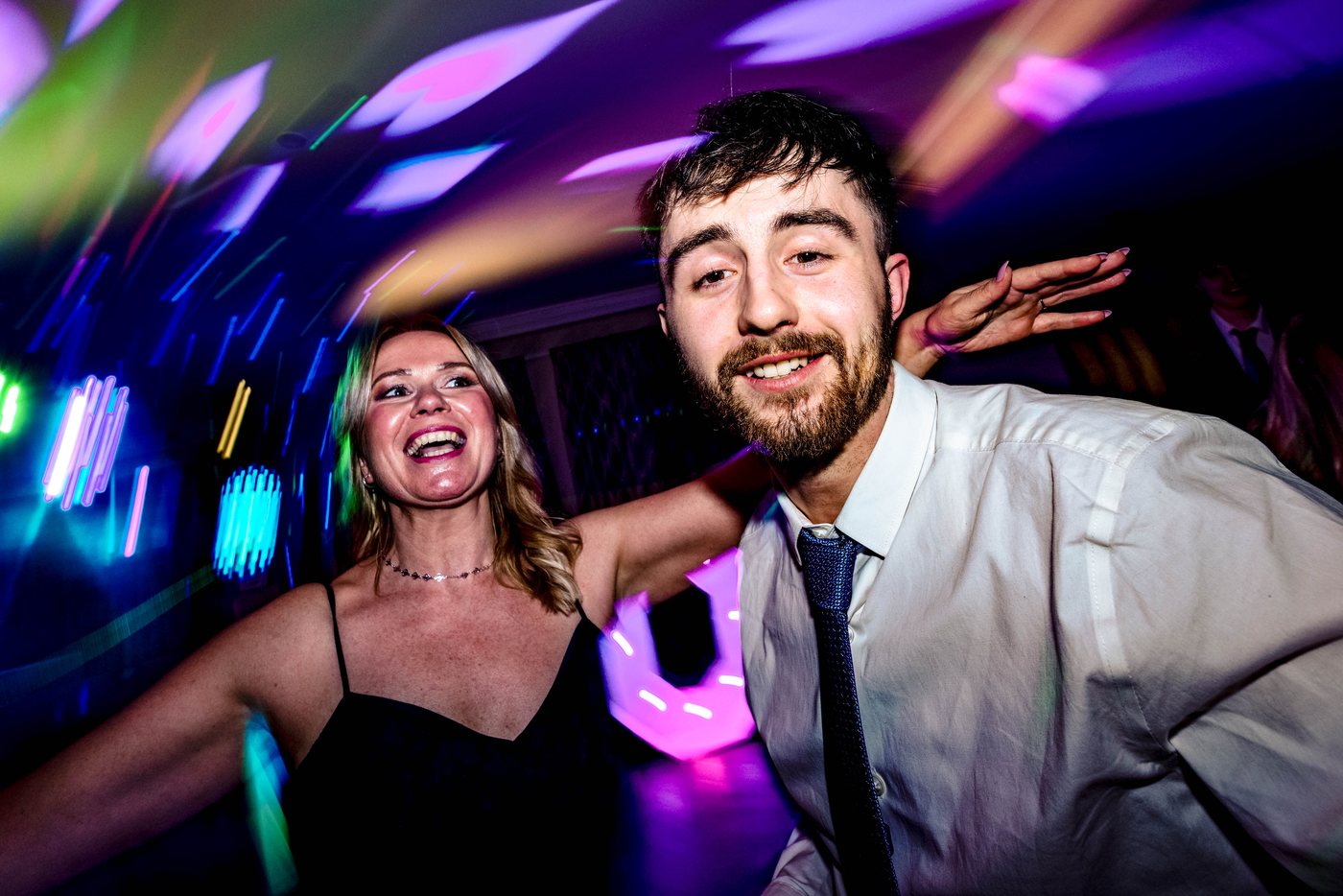 Two guests dancing with their arms out, lit by the DJ lights